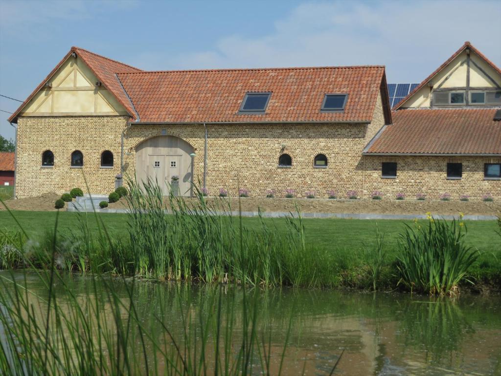 a large brick building with a white door next to a pond at Hoeve Lavigne in Wellen