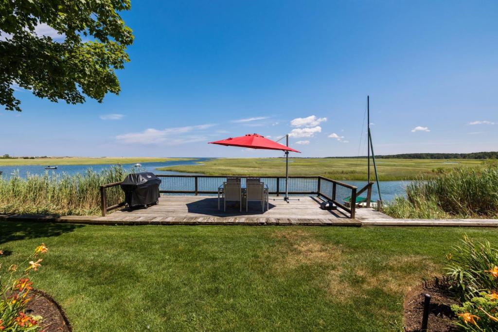 a patio with a table and an umbrella next to a lake at 7 Sunrise Lane Sandwich Cape Cod - - Sunrise Vista in Sandwich