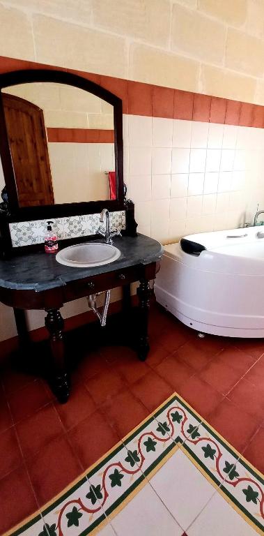 a bathroom with a sink and a tub and a mirror at Ta Majsi farmhouse with indoor heated pool in San Lawrenz