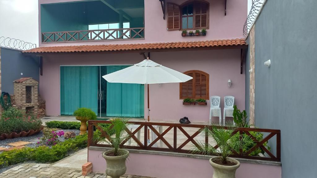 ein rosafarbenes Haus mit Sonnenschirm und Balkon in der Unterkunft Casa de Serra Vila Viçosa in Viçosa do Ceará