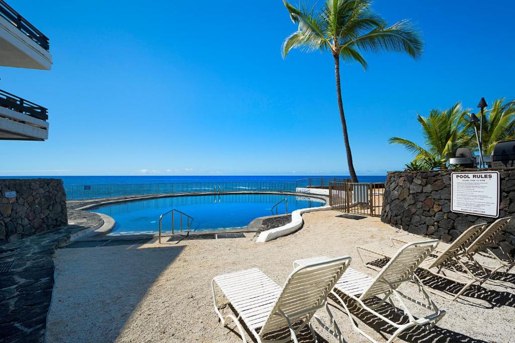 a pool with chairs and a palm tree and the ocean at Casa De Emdeko 104 in Kailua-Kona