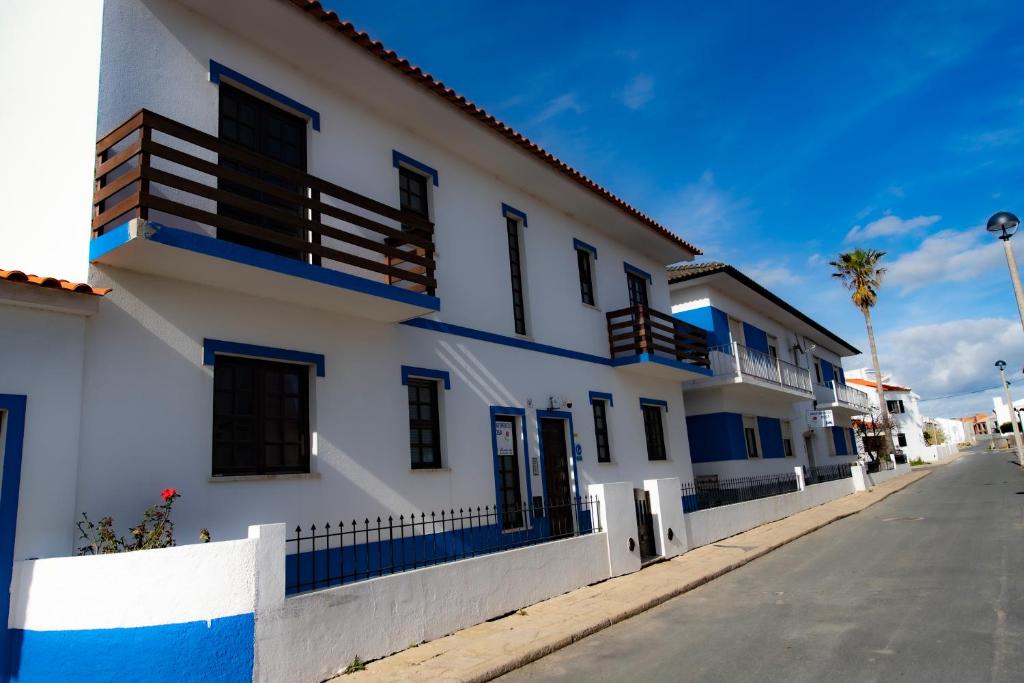 a white building with blue accents on a street at Apartamento Rosa in Porto Covo