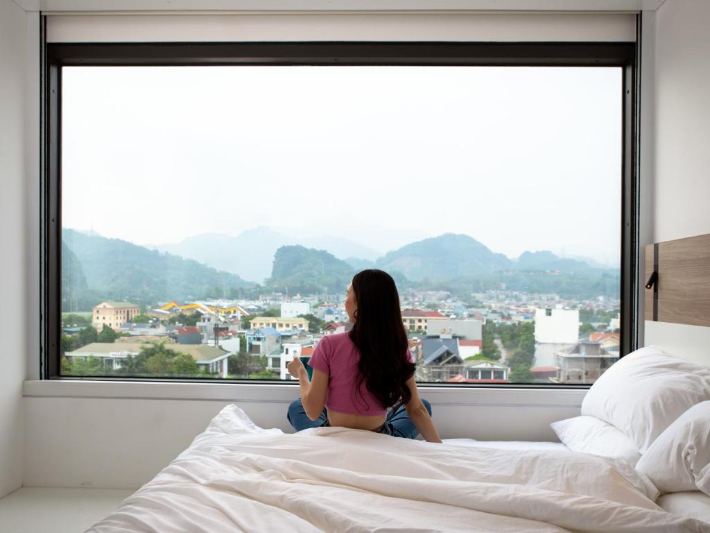 uma mulher sentada numa cama a olhar pela janela em SOJO Hotel Hoa Binh em Hòa Bình