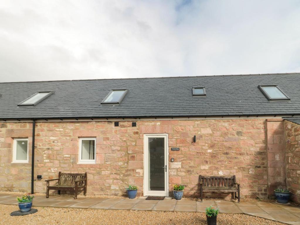 a stone house with two benches and solar panels at Yeavering in Wooler