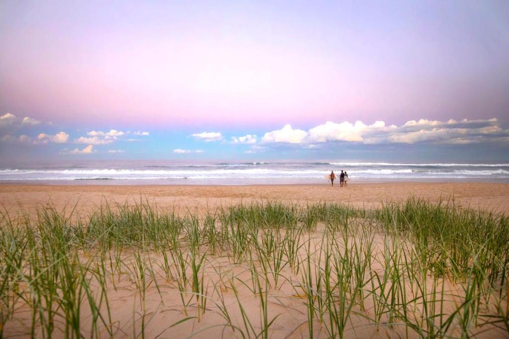 two people walking on a beach near the ocean at 1 Horizon Terraces Beautifully Styled Duplex Perfect Beach Vibes in Sunshine Beach