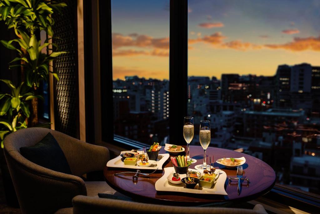 Okinawa Harborview Hotel في ناها: طاولة مع طعام وكؤوس للنبيذ في غرفة مع نافذة