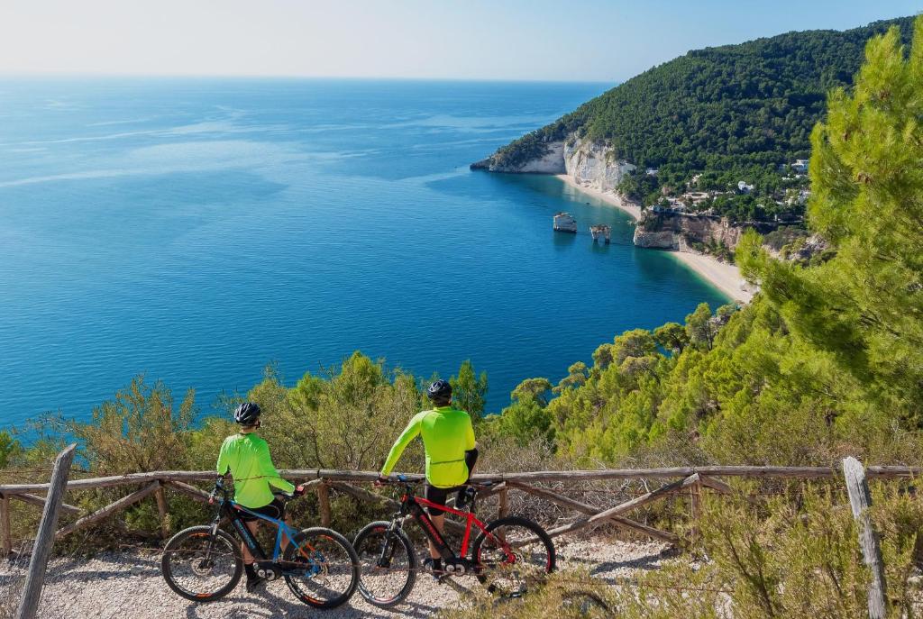 duas pessoas a andar de bicicleta numa colina com vista para o oceano em Case Vacanze Uliveto em Mattinata