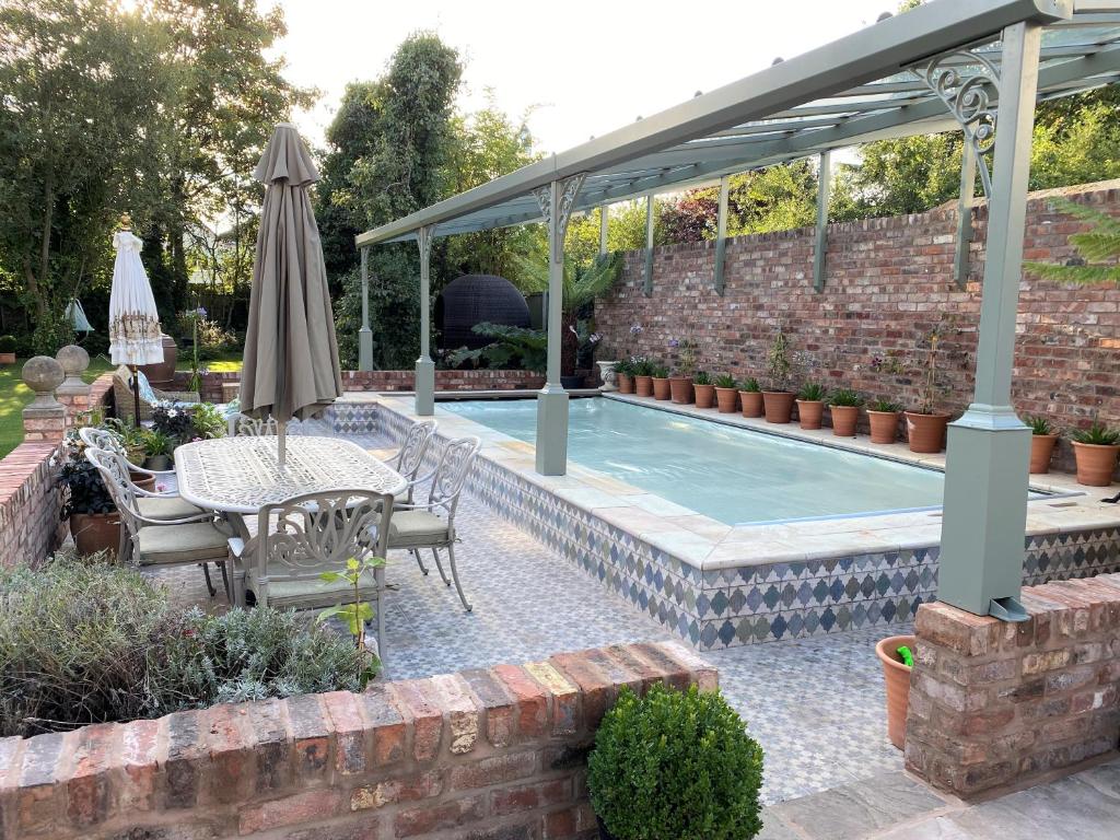 a patio with a table and an umbrella and a pool at Lyndhurst - Victorian villa with heated pool in Roby