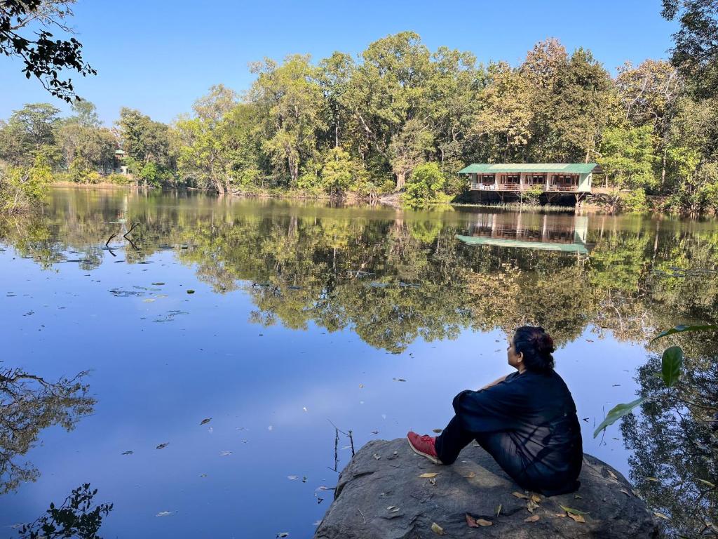 una mujer sentada en una roca frente a un lago en Rukhad Jungle Camp - Pench, 