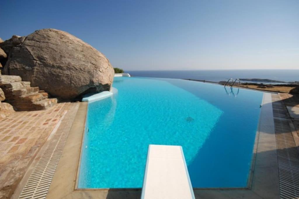 a large blue swimming pool with a large rock at Nefeli Sea View Holiday House in Mýkonos City