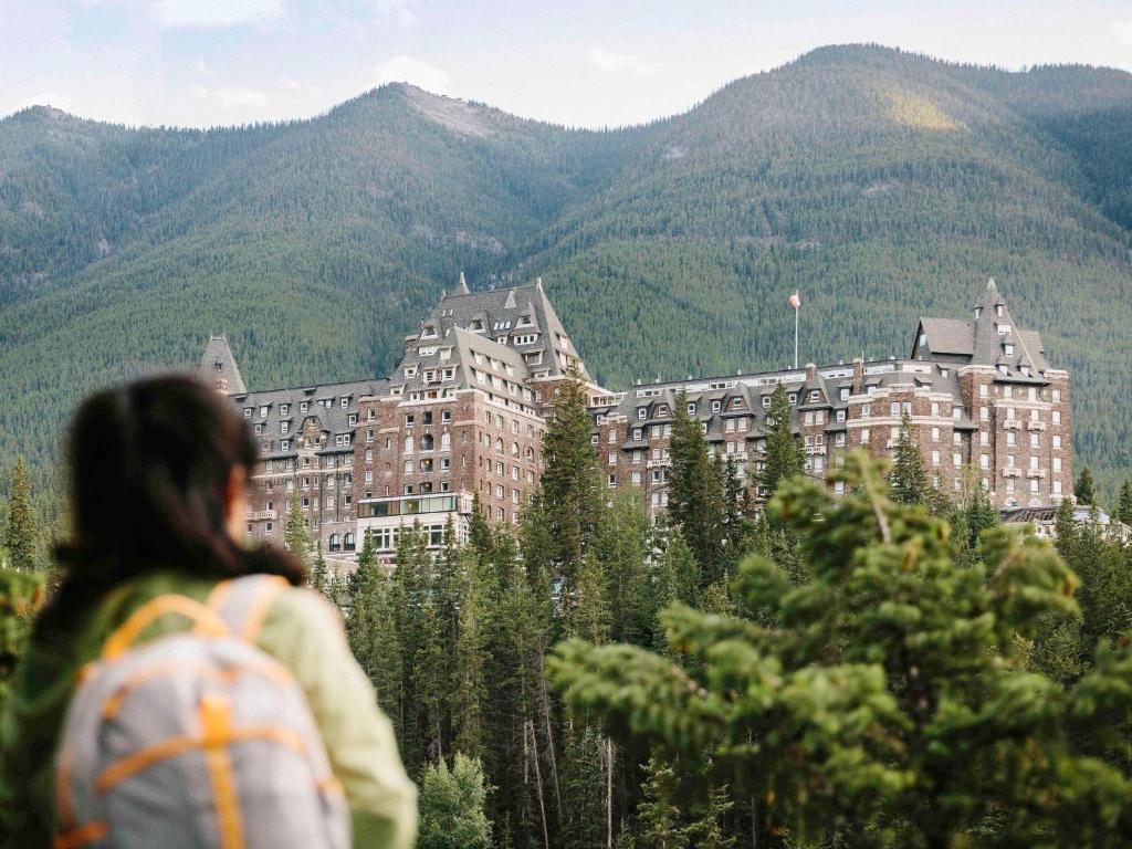 a woman with a backpack looking at a building in the mountains at Fairmont Banff Springs in Banff