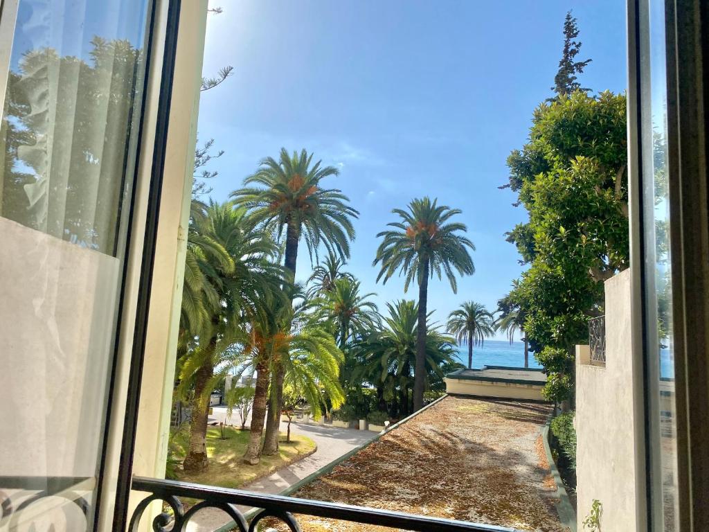 a window with a view of the ocean and palm trees at "Le Regina", Vue Mer, Plein Centre, Unique in Menton