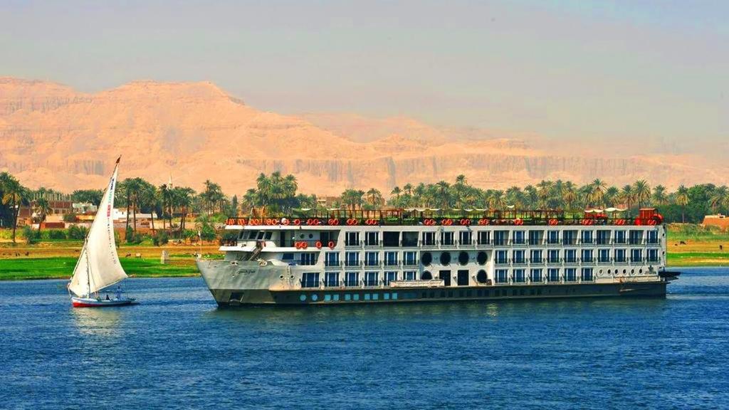a large cruise ship on the water with a sailboat at Nile cruise Aswan To Loxur 3 Nigh in Aswan