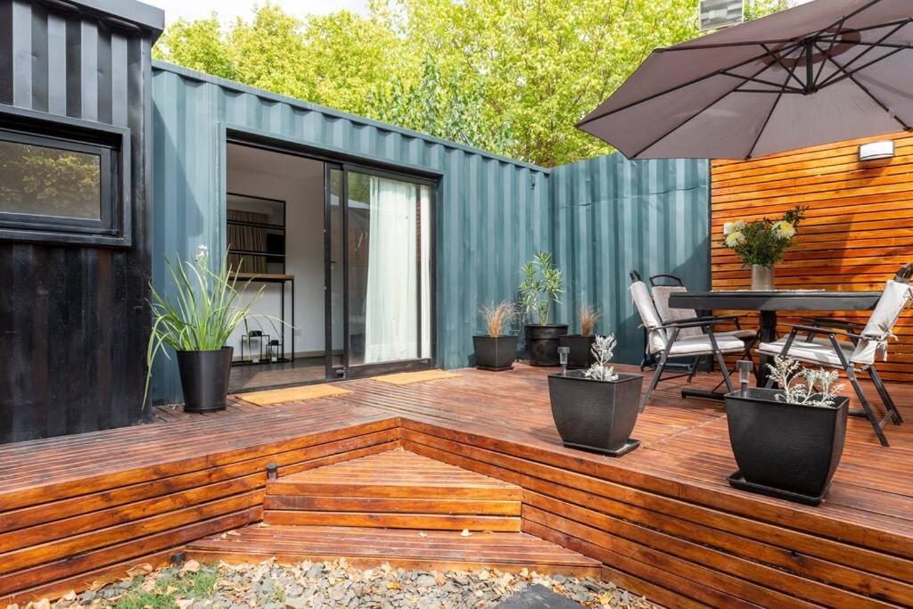 una terraza de madera con mesa y sombrilla en Aromos Lodge- Chacras de Coria- en Luján de Cuyo