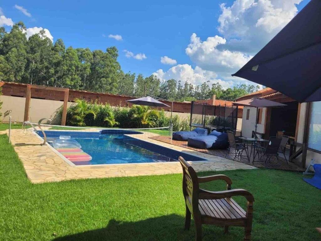 un patio con piscina con banco y sombrilla en Linda Casa de Campo Nova em condomínio, en Porangaba