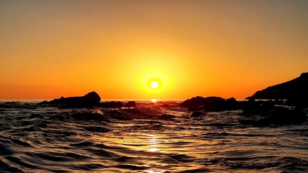 a sunset over the ocean with rocks in the water at San Giuseppe Casa per Ferie in Quercianella