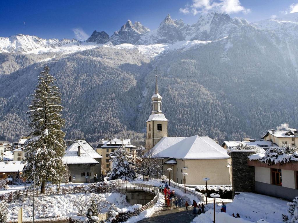 a snowy village with a church and mountains in the background at Chalet Evasion by Interhome in Les Bossons
