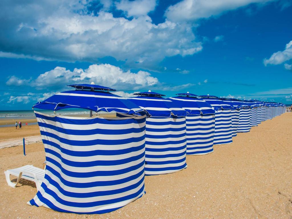a row of blue and white striped umbrellas on a beach at Apartment Le Chalet by Interhome in Cabourg