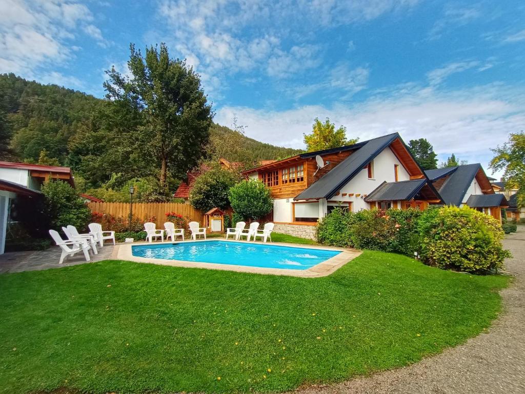 een achtertuin met een zwembad en stoelen en een huis bij Cabañas Los Alamos by Visionnaire in San Martín de los Andes