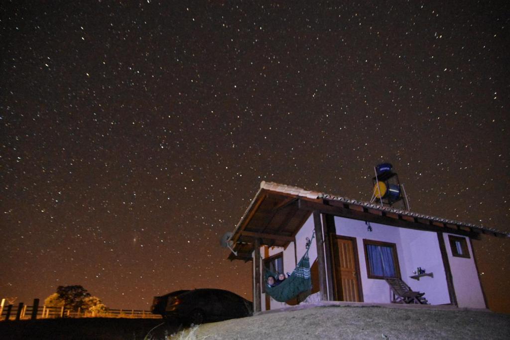 Un uccello seduto sopra una casa sotto un cielo stellato di Pousada Gaya a Carrancas
