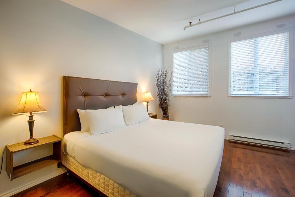 ein Schlafzimmer mit einem großen weißen Bett und zwei Fenstern in der Unterkunft Les Lofts St-Jo - Par Les Lofts Vieux-Québec in Québec