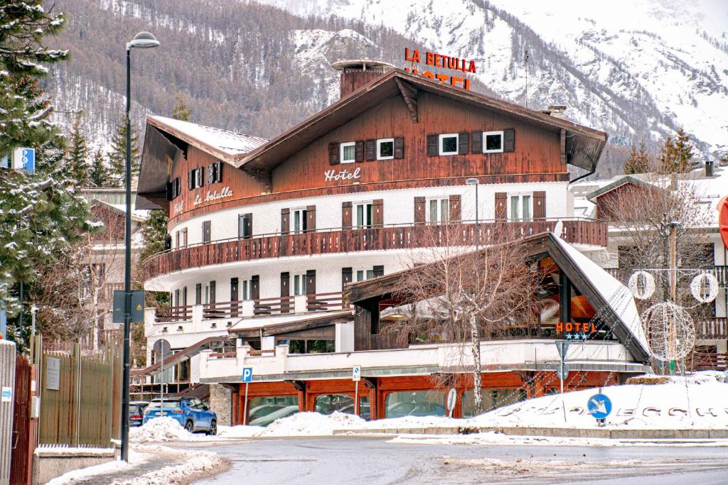 un gran edificio en una calle nevada con una montaña en Hotel La Betulla, en Bardonecchia