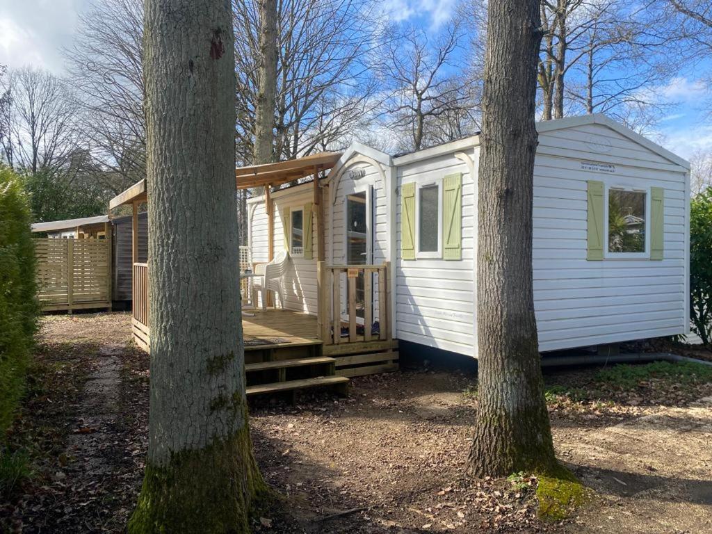 Une petite maison blanche dans les bois entre deux arbres dans l'établissement mobil-home au Parc des roches, à Saint-Chéron