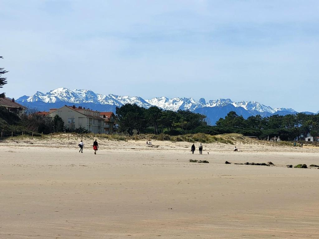 a group of people walking on a beach with snow covered mountains at Apartamentos San Vicente Playa in San Vicente de la Barquera