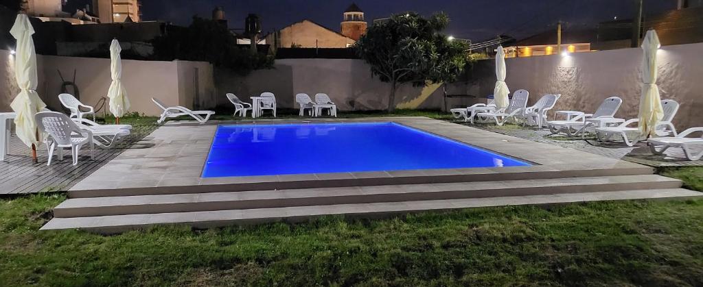 uma piscina num quintal com cadeiras brancas em Hotel El Velero em Villa Gesell