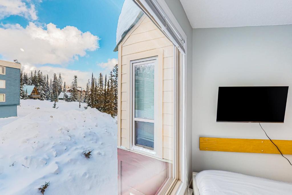 a bedroom with a window with a tv and snow at Whitefoot Lodge 314 in Big White