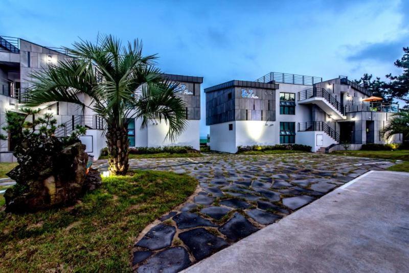 a large house with a palm tree in front of it at Sea and Wave in Seogwipo