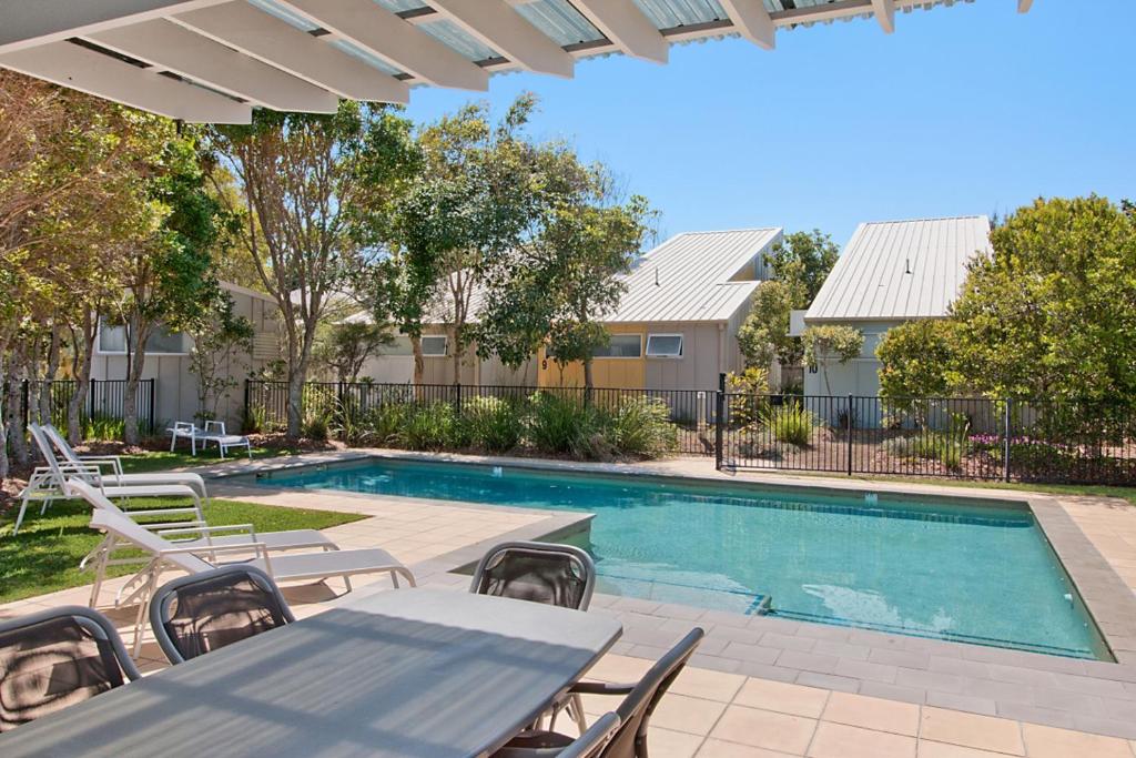 a swimming pool with a table and chairs next to a house at Pandanus Pocket 3BR Beachside Condo by uHoliday in Casuarina