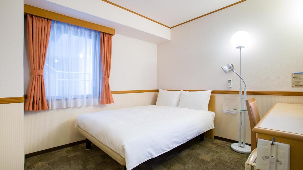 Toyoko Inn Okinawa Naha Kokusai-dori Miebashi-eki في ناها: غرفة نوم بسرير أبيض ونافذة