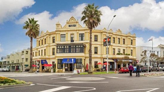 een groot geel gebouw met palmbomen voor een straat bij The Esplanade Hotel in Auckland