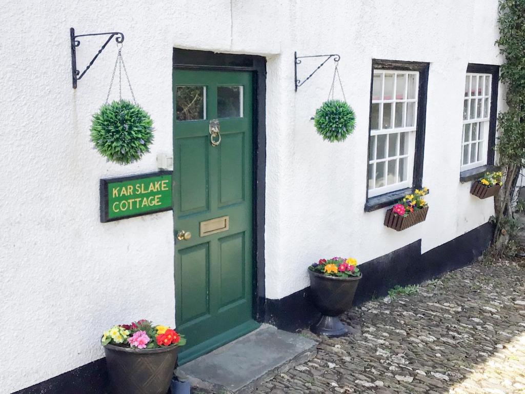 Karslake Cottage في Winsford: باب أخضر على مبنى أبيض به نباتتين خزاف