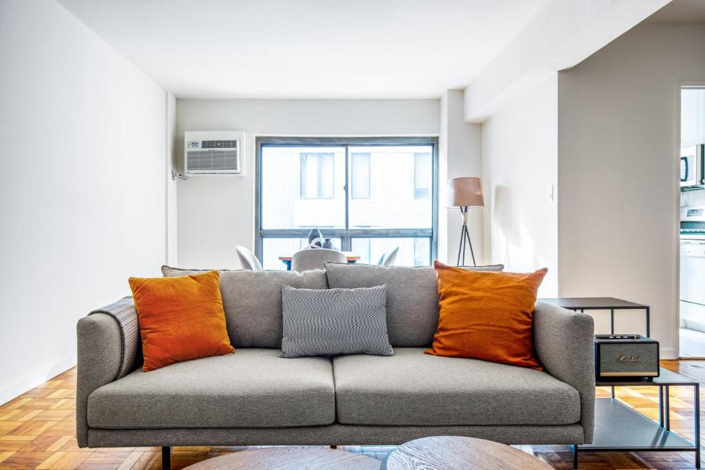 ein Wohnzimmer mit einem Sofa und orangefarbenen Kissen in der Unterkunft Midtown E 1BR w WD Doorman nr Central Park NYC-532 in New York