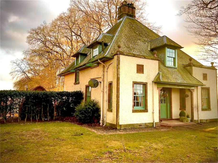 uma antiga casa branca com um telhado verde em A charming, well appointed Edwardian Gate Lodge em Alyth