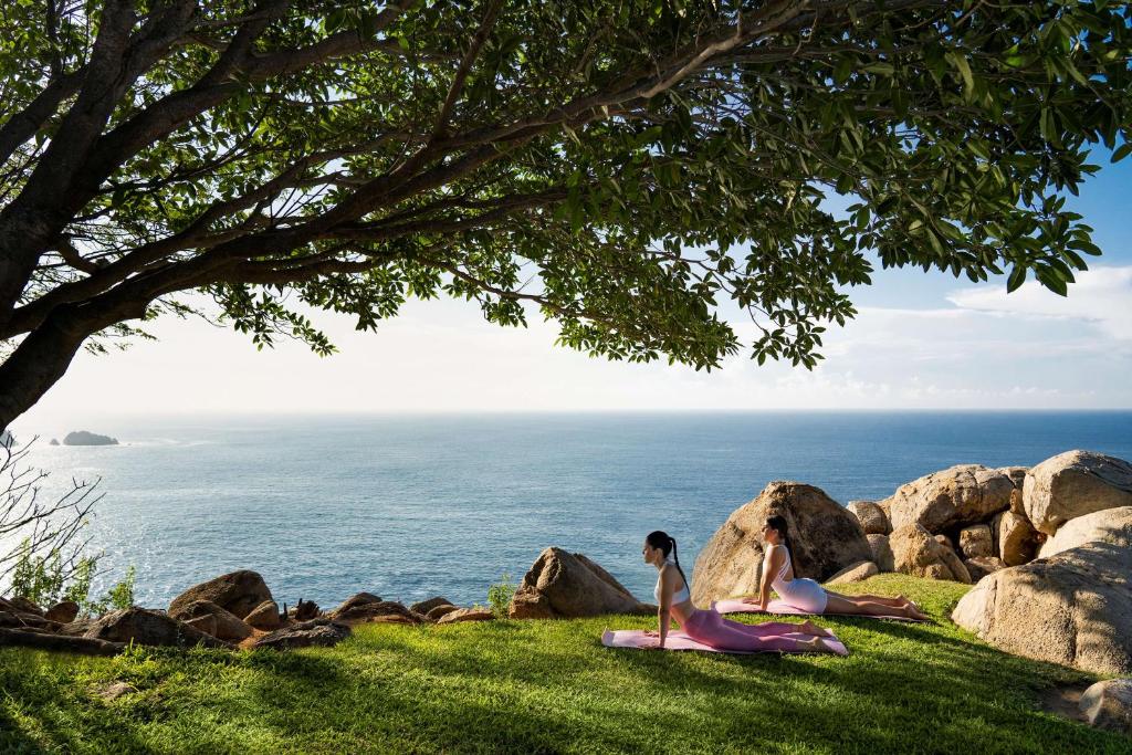 two girls sitting on the grass near the ocean at Banyan Tree Cabo Marques in Acapulco