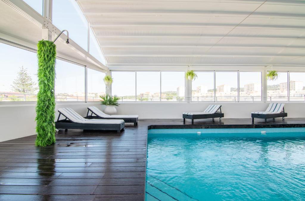 una piscina en una habitación con sillas y una piscina en Loule Jardim Hotel, en Loulé