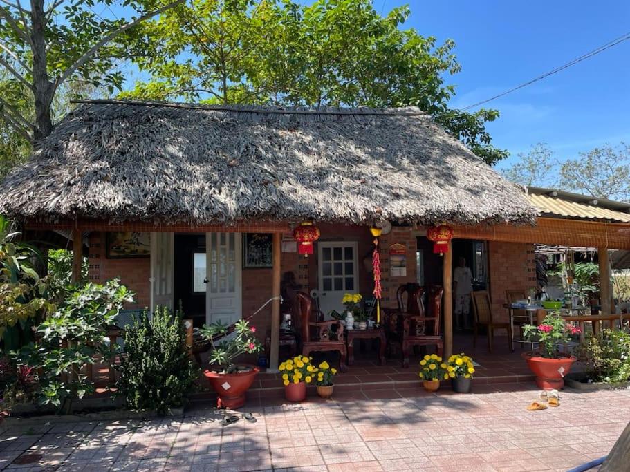 a small house with a thatched roof and a patio at Ty Phu Miet Vuon Homestay - Entire Bungalow in Tây Ninh