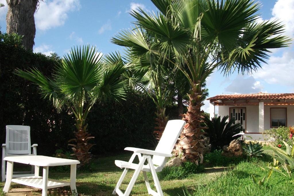 two white chairs and palm trees in front of a house at Villa Davima in Marzamemi