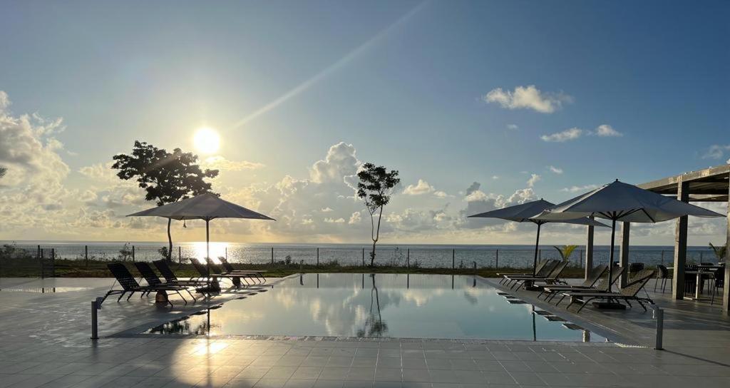 a swimming pool with chairs and umbrellas and the ocean at Ibis Styles Mayotte Aéroport in Pamandzi