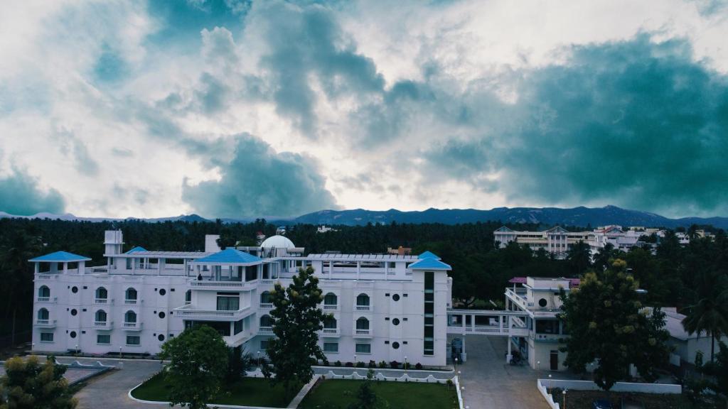 a large white building with a cloudy sky in the background at Hotel Agni in Krishnagiri