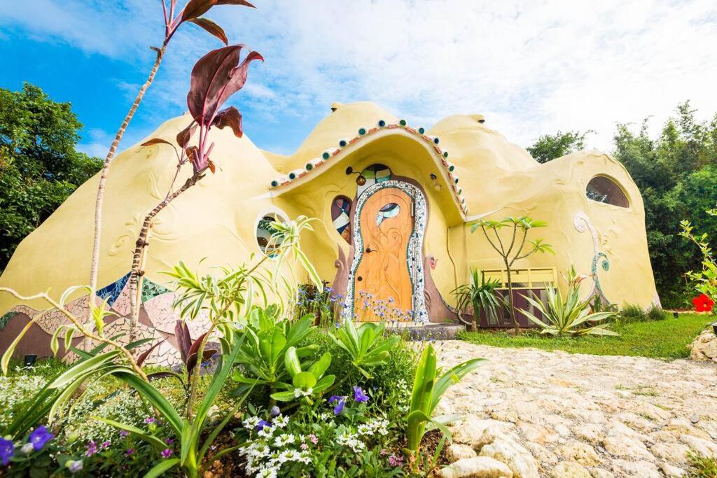 a house shaped like a home with flowers in front of it at 土と音の旅チオンの家 in Onna