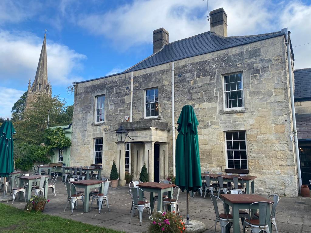 un antiguo edificio de piedra con mesas y sombrillas delante de él en The Castle Inn Bradford on Avon en Bradford on Avon