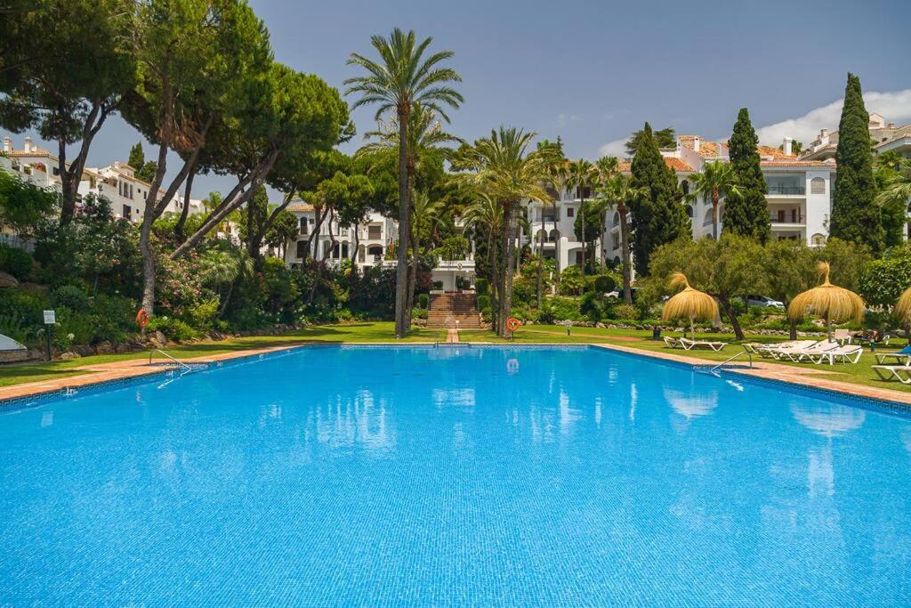 una gran piscina azul con palmeras y edificios en Luxury stay near Puente Romano, always Heated Pool 5*, en Marbella
