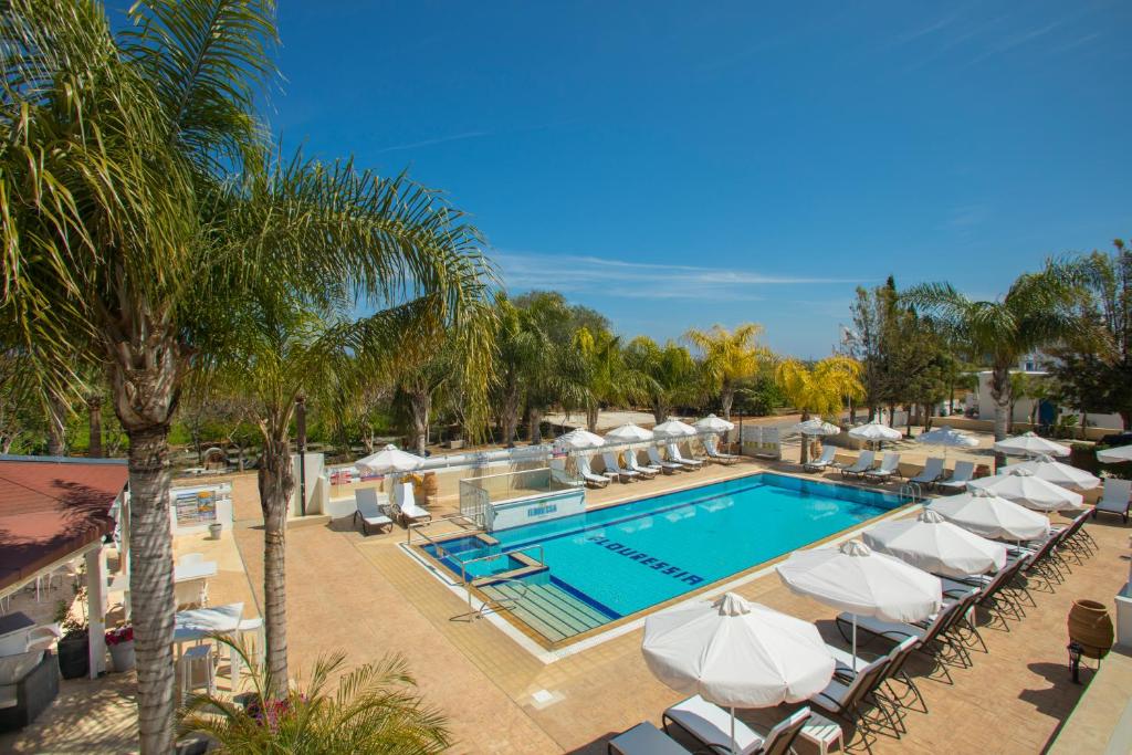 a pool with white umbrellas and lounge chairs at Flouressia Gardens in Protaras