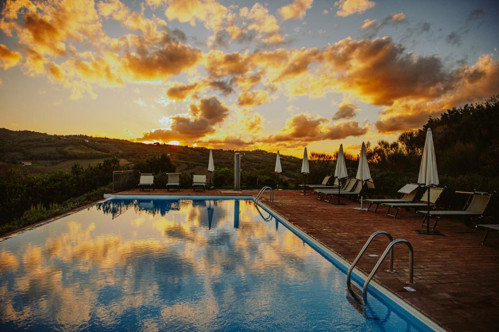 a swimming pool with chairs and umbrellas and a sunset at Tenuta Pianirossi in Cinigiano