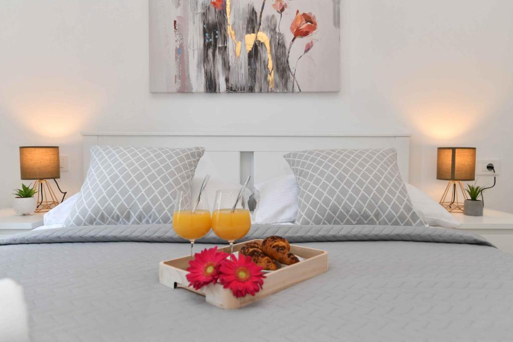 a tray with two glasses of orange juice and flowers on a bed at Apartman Leona in Lovran