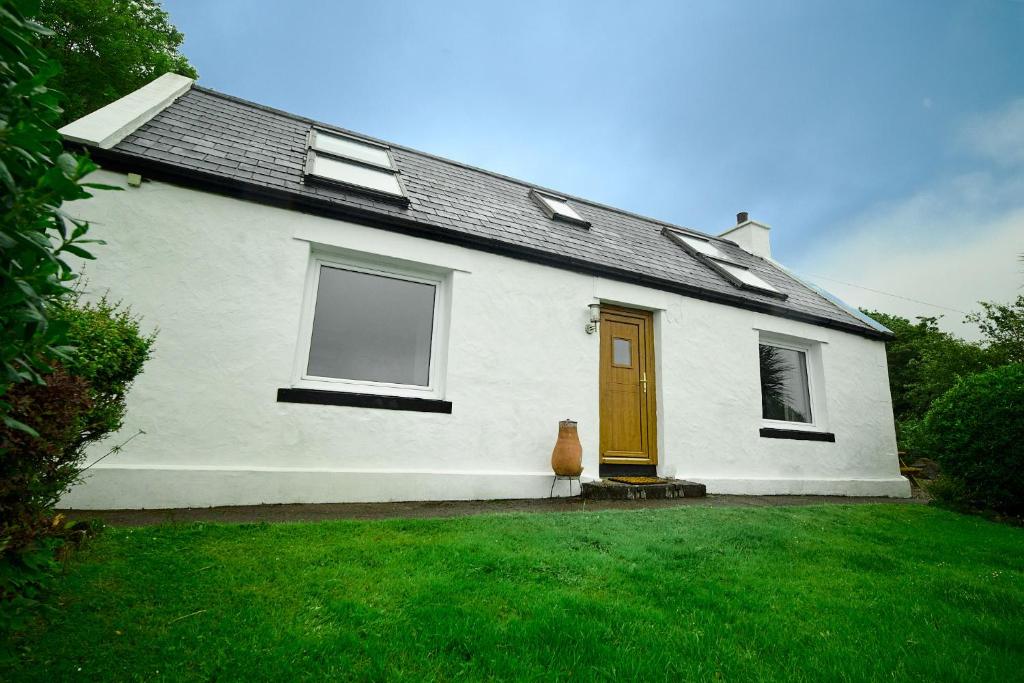 a white house with a brown door and a yard at Hawthorn Cottage in Uig